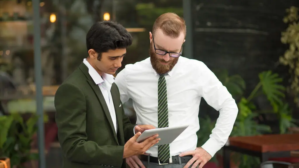 Zwei Männer im Gespräch über eine Karriereseite auf dem Tablet – Symbolbild für modernes Recruiting, umgesetzt von der Design und IT Agentur aus Herford snutig.